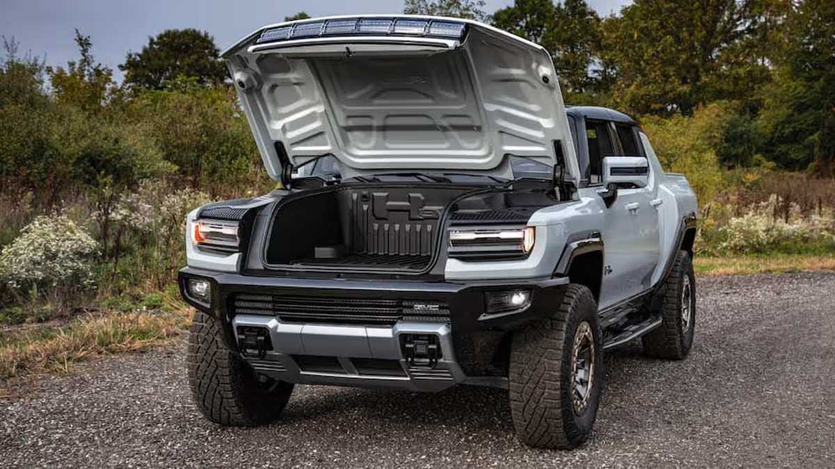 A Hummer EV with its hood raised, showcasing a spacious front trunk area against a natural background. 