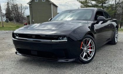 A 2025 Dodge Charger EV with red brake calipers parked on gravel, surrounded by green grass and trees in the background.