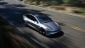 A silver Tesla Model 3 Performance speeds down a winding road, surrounded by lush greenery, showcasing its sleek design and dynamic motion.