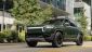 A sleek green electric SUV drives past modern buildings, showcasing its distinctive design and eco-friendly appeal.