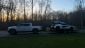 White Rivian R1T towing a trailer with a McLaren at sunset, surrounded by bare winter trees